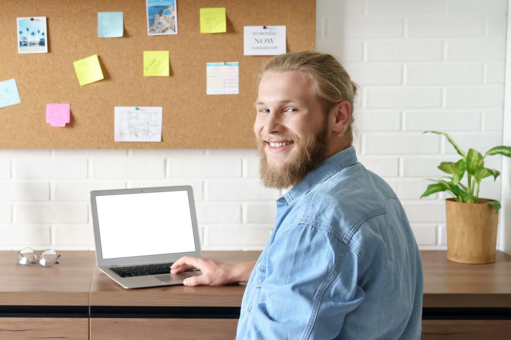 smiling young bearded man student remote worker working studying from home office online on laptop computer sit at desk