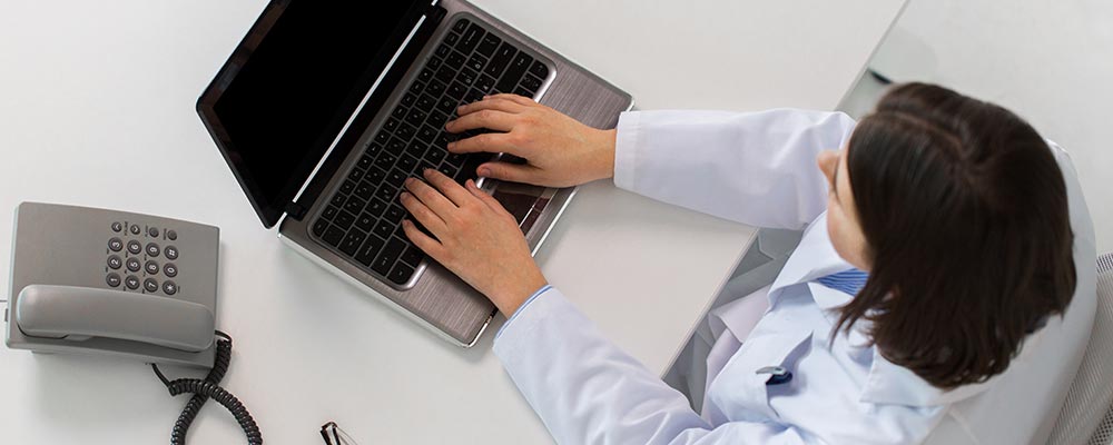 medicine, healthcare and people concept - woman doctor with prescription typing laptop computer sitting at table in clinic